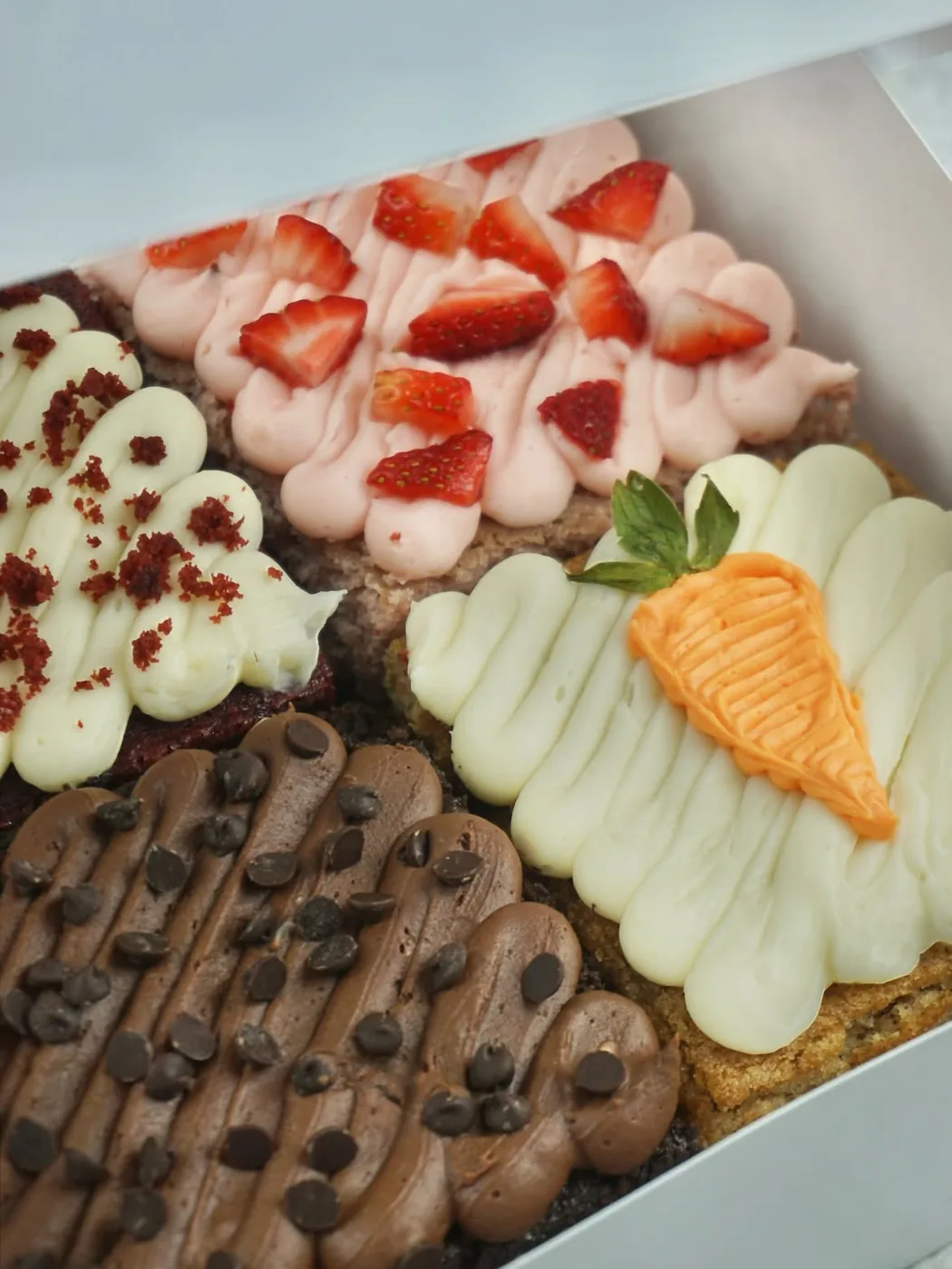 Close up of the decorated bars, buttercream piped in rows and finished with sliced strawberries, chocolate chips and a piped carrot