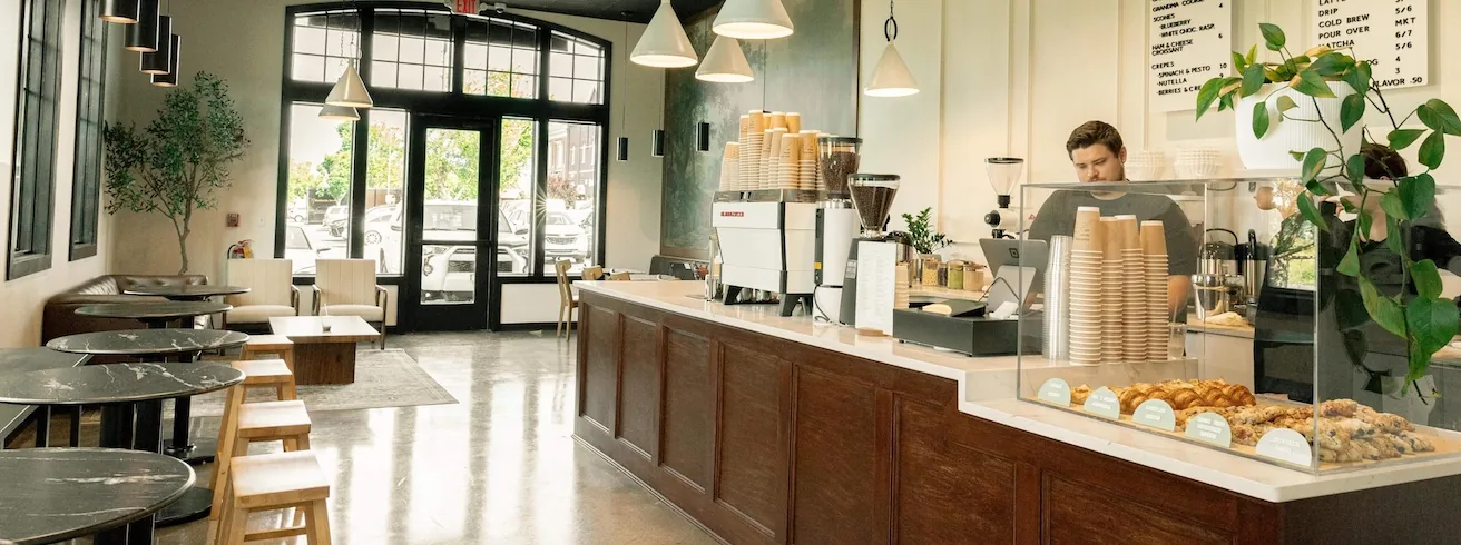 Inside Morning Brew Co on Cambridge Square, the long wooden counter with the espresso machine, and the glass bakery case of pastries at the far end