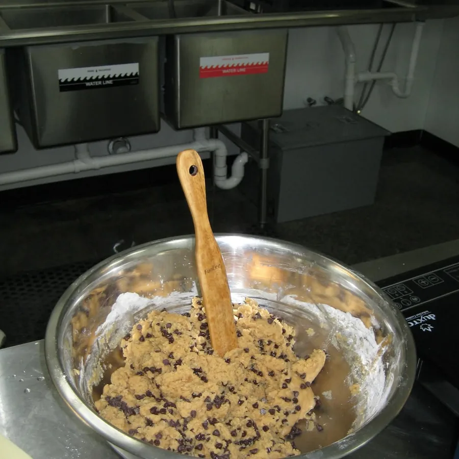 A steel bowl of chocolate chip cookie dough being mixed in the back kitchen