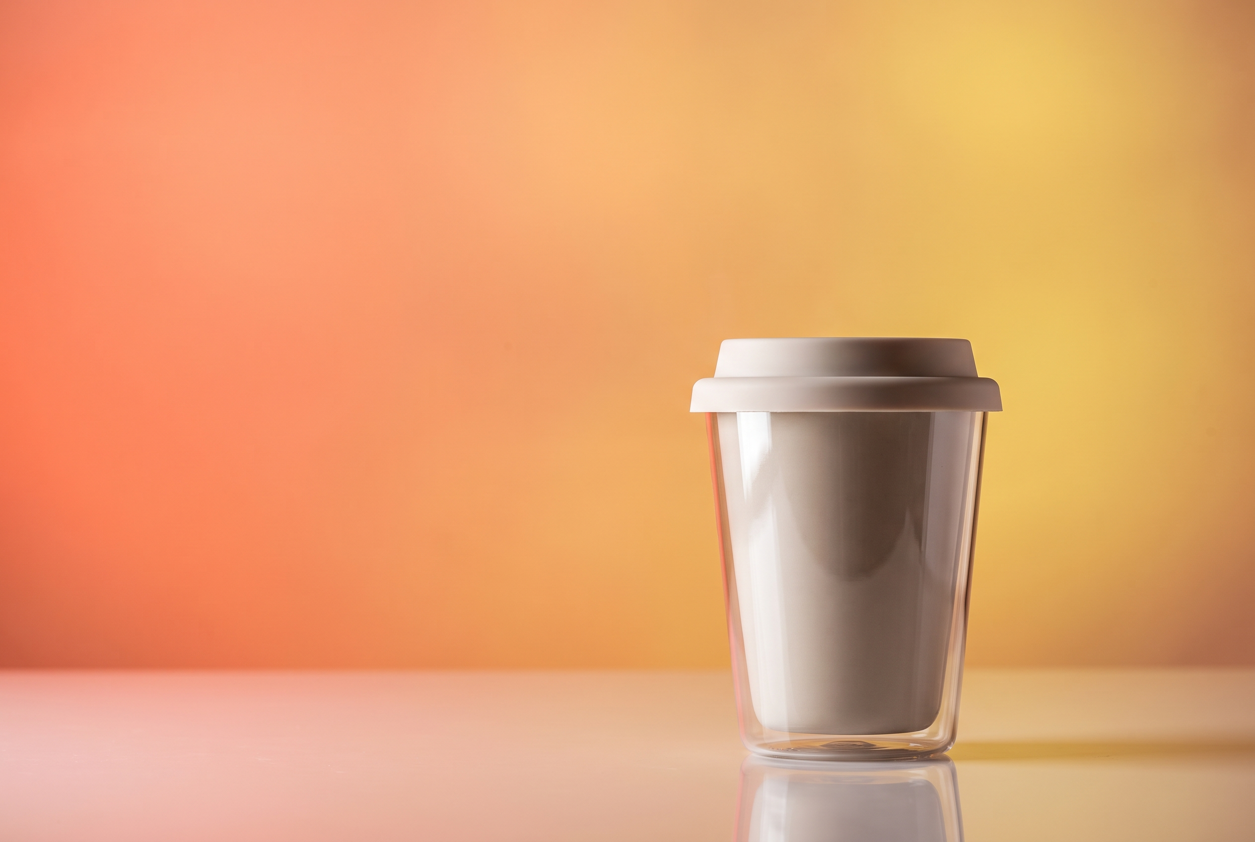 Glass to-go cup of fresh latte glowing against a coral and gold gradient