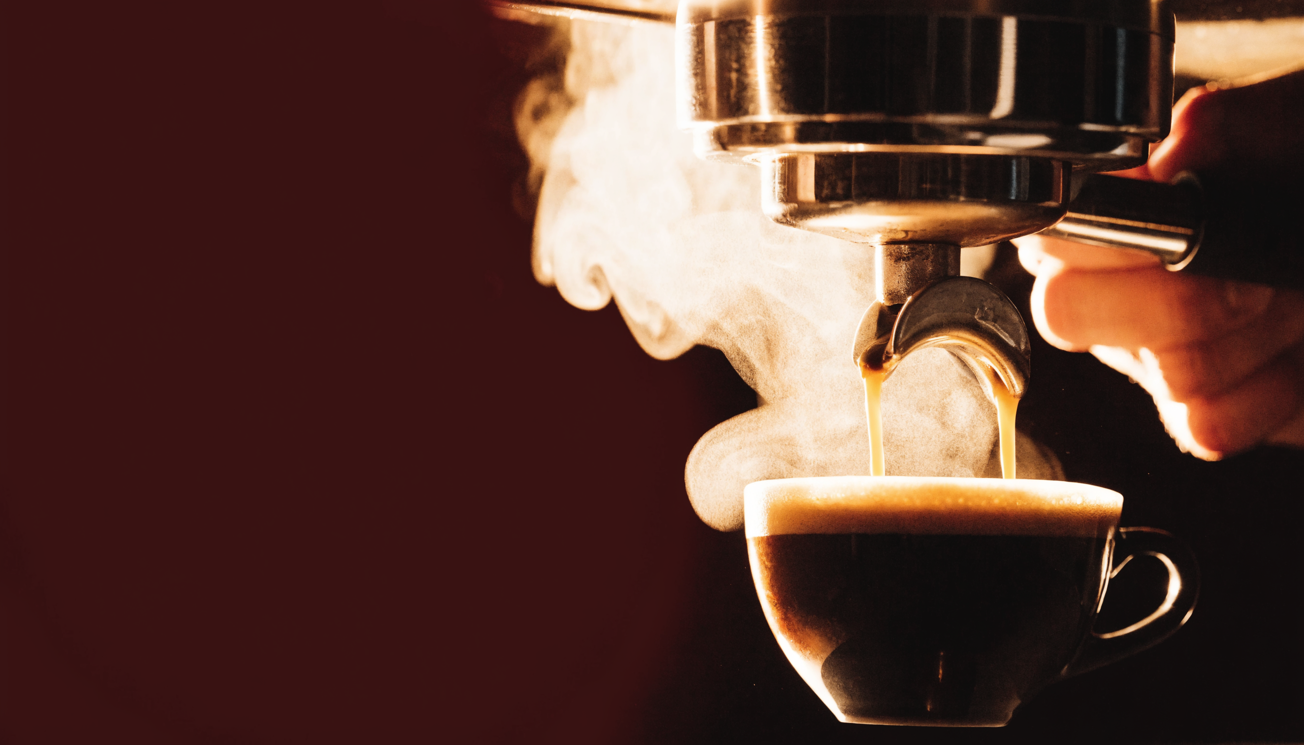 Espresso pulling from a portafilter into a cup, steam lit gold against a dark room